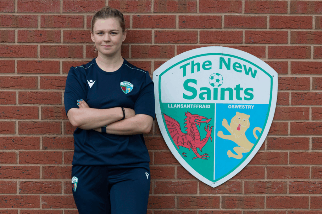 Jodie Williams poses in a TNS shirt next to The New Saints badge